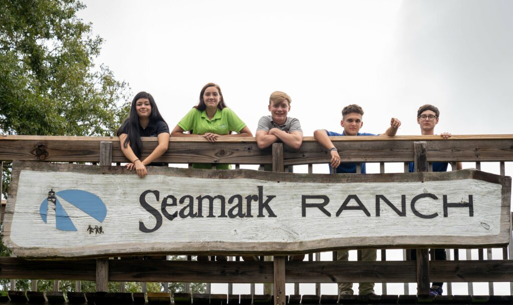 Several children standing behind a sign that says seamark ranch